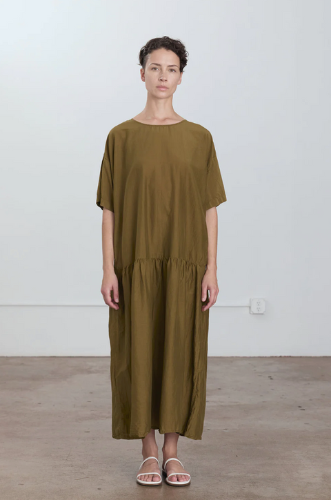 Woman wearing a green dress standing against a white wall.