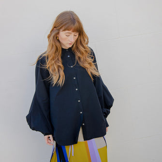 Woman wearing black cotton loose fitting shirt with balloon shaped sleeves. Featuring collar, button through front and cuffs.