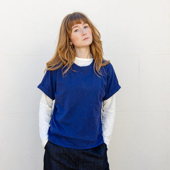 Woman wearing blue linen blend basic t-shirt with rolled sleeves and round neckline.