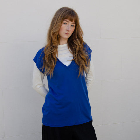 Woman wearing bright blue fluid jersey top with cap sleeves and V-neck.