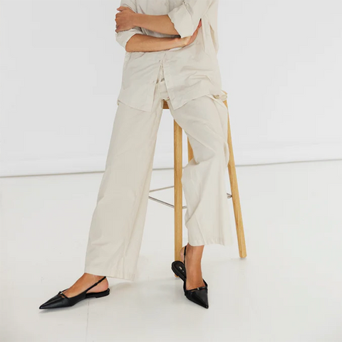 Model wearing cream organic cotton drawstring trousers with wide legs and side pockets.