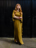 Woman wearing long gold colour dress in shiny and matte fabric. Featuring front tie detail, side slits and half button front.