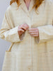 Woman wearing light checked cream jacket. Loose fitting with pockets and styled with t-shirt and linen trousers.