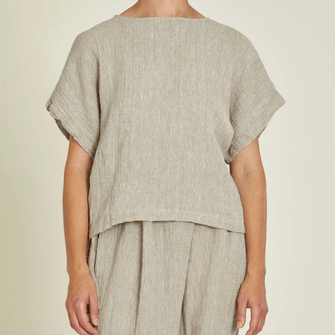Woman wearing natural coloured textured linen top. Loose fitting with round neckline and short sleeves.