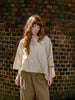 Woman wearing oversized silky linen top. Slight shimmer to the fabric and sand colour with crew neck and three quarter length sleeves.