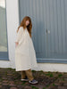 Women wearing cream tennis style dress. Made from cotton and linen mix. Oversized body and buttons at the neckline.